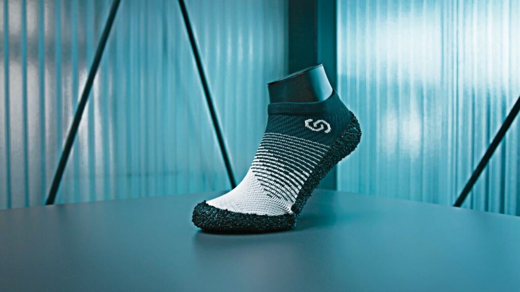 Skinners 2.0 sock shoe standing on a blue studio floor