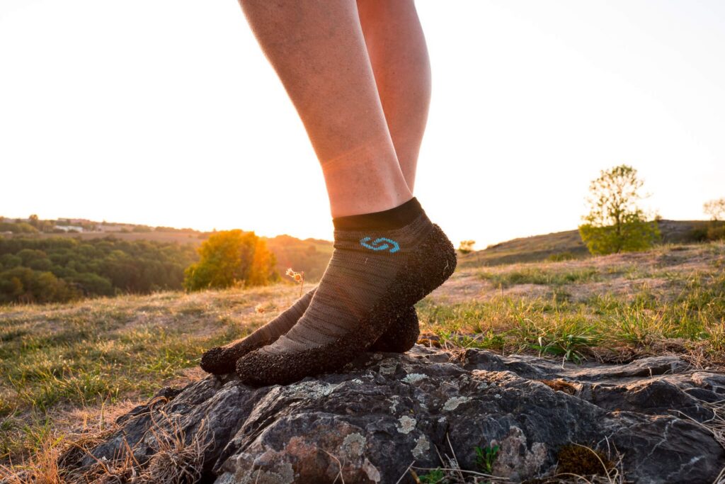 Feet in Skinners sock shoes on a rock at sunset